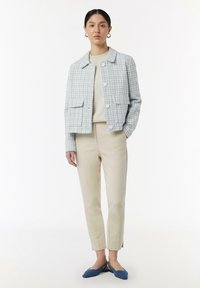 Lichtblauwe en witte geblokte jas van textuurstof, gecombineerd met een beige top en op maat gemaakte crèmekleurige broek. Blauw flats maken de outfit af.