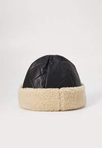 Chapeau en cuir matelassé noir avec une bande en shearling beige à la base. Forme arrondie, texture lisse sur le dessus, texture douce sur le dessous.