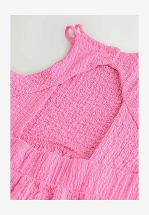 Vaaleanpunainen teksturoitu mekko, jossa on smokkaukset, pyöreä pääntie ja napillinen kiinnitys sekä pienet silmukat olkaimissa.