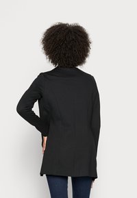 Czarna marynarka dopasowana, z długimi rękawami, o taliowanym kroju i jednym rozcięciem z tyłu. Gładka faktura i minimalistyczny styl.