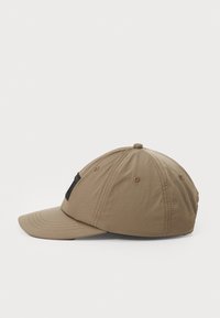 Khaki caps med buet skygge, med svarte mesh-detaljer, sømdetaljer og en rund krone med ventilasjonsøyer.