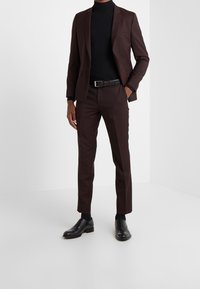 Donkerbruine op maat gemaakte kostuum met slim-fit broek, zwarte coltrui en zwarte schoenen. Heeft een minimalistisch ontwerp en een gladde stofstructuur.