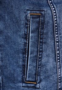 Blå denimtyg med en rektangulär ficka med kontrasterande guldstickning och slät textur, framhävd av en ren, strukturerad design.