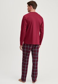 Rode langemouwtop gecombineerd met een geruite slaapbroek in rood, zwart en wit. De stof lijkt lichtgewicht met een gladde textuur.