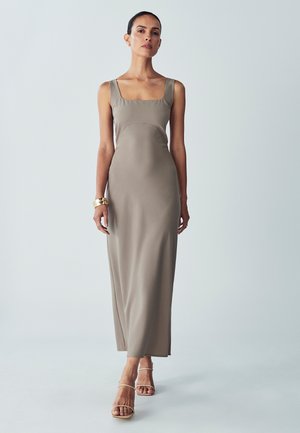 Vestido largo y ajustado de tela suave color topo, con escote cuadrado, tirantes anchos y diseño minimalista, combinado con sandalias beige con tiras.