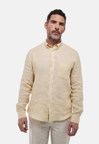 Chemise en lin à manches longues de couleur jaune clair, avec un col à boutons, une poche poitrine unique et une coupe décontractée avec une finition texturée.