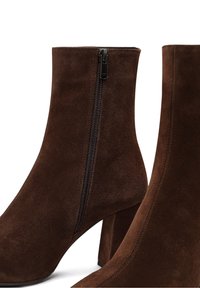 Bottes cheville en daim marron avec talons blocs et fermetures éclair latérales, présentées de profil sur fond blanc.