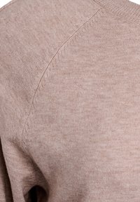 Nærbillede af blødt beige strikstof med synlig søm og fin ribstrikket tekstur på et tøjs skulderområde.