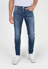 Jeans skinny de denim azul oscuro con un acabado desgastado. Cuenta con un clásico diseño de cinco bolsillos y un pequeño logo en la parte posterior.