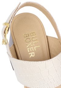 Sandale en cuir blanc gaufré crocodile avec une semelle intérieure beige. Dotée d'une boucle dorée et du logo doré "BULL BOXER" sur la semelle intérieure.