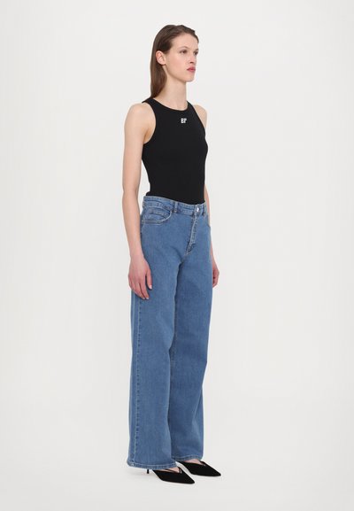 Black sleeveless bodysuit, high neckline, paired with light blue high-waisted wide-leg jeans. Slim-fit silhouette with minimal detailing.