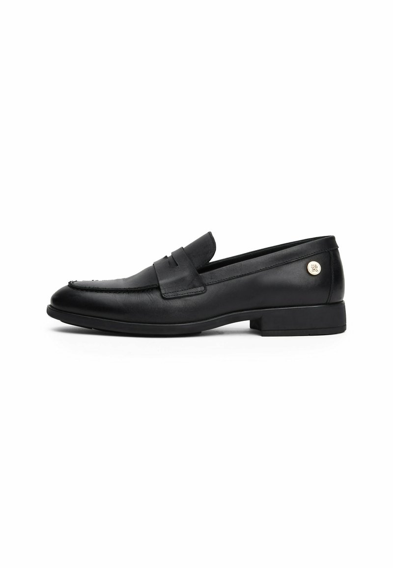Mocassins en cuir noir à semelle plate, présentant un bout effilé, des détails cousus, une bride décorative et un accent métallique de marque.