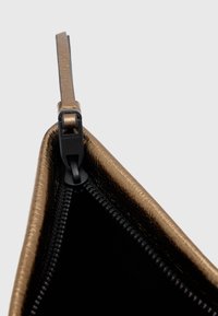 Bronsfärgad handväska i konstläder med svart insida, försedd med dragkedja och ett platt handtag. Ytan har en subtil textur.