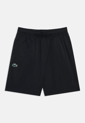 Schwarze Sportshorts mit elastischem Bund und kleinem grünem Krokodil-Logo am linken Bein vor einfarbigem Hintergrund.