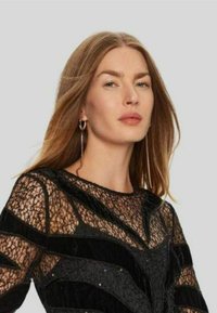 Abito nero con pizzo trasparente e motivi geometrici, accentuato da dettagli in velluto. Il design include sottili decorazioni e orecchini lunghi.