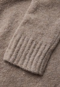 Gros plan sur un pull en laine marron, mettant en avant un tissu texturé et doux avec un détail de poignet côtelé, affichant une couleur chaleureuse et neutre.