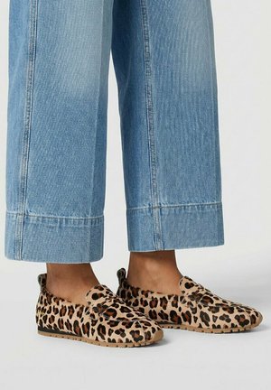 Voeten met lichtblauwe cropped jeans en loafers met luipaardprint en rubberen zolen op een lichtgrijze vloer.