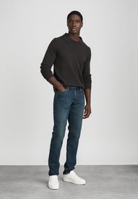 Ciemnobrązowa bluzka polo z długim rękawem, dżinsy w niebieskim odcieniu i białe sneakersy; swobodny strój o prostym kroju.