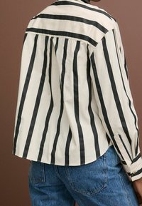 Stribet skjorte med sorte og cremefarvede lodrette striber, letvægtsstof, en afslappet pasform og knapmanchetter med en let hale bagpå.