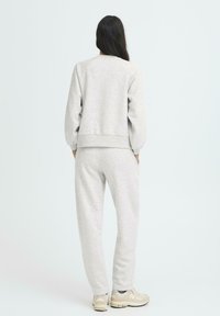 Sudadera de algodón gris claro y pantalones a juego. Corte relajado, con puños y dobladillo acanalados, y bolsillos laterales en los pantalones. Textura suave y neutra.