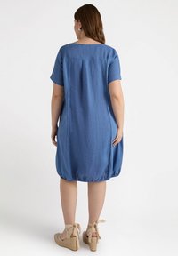 Blå linnklänning med korta ärmar, rynkad nederkant och sidofickor. Matcher med beige kilklack-sandaler med ankelsnören.