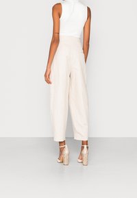Light beige linen trousers with a relaxed fit, featuring side pockets and a high waist, paired with beige and snakeskin high-heeled shoes.