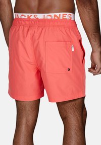 Pantaloni da bagno corallo con vita elastica e logo "JACK & JONES". Include una tasca posteriore con un dettaglio a bottone a contrasto.