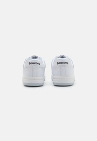 White leather sneakers with a textured finish, featuring a padded collar, flat laces, and a prominent black “Saucony” logo on the heel.