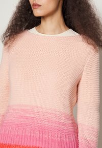 Sweter robiony na drutach w delikatnym różowym gradiencie, przechodzącym od jasnych do ciemniejszych odcieni, z prążkowanym dołem i okrągłym dekoltem. Teksturowana tkanina.