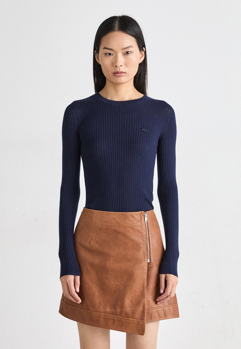 Maglietta a maniche lunghe a coste blu navy con collo a girocollo abbinata a una mini gonna in pelle marrone con chiusura laterale e orlo a contrasto.