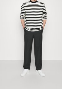 Svetr s černobílým pruhem a kulatým výstřihem, kombinovaný s černými kalhotami a bílými teniskami. Oble�čení má uvolněný střih.