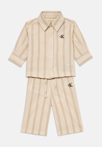 Béžová a krémová vertikálne pruhovaná košeľa s krátkym rukávom na gombíky a zodpovedajúce šortky na šnúrku s logami CK na hrudi a stehne.