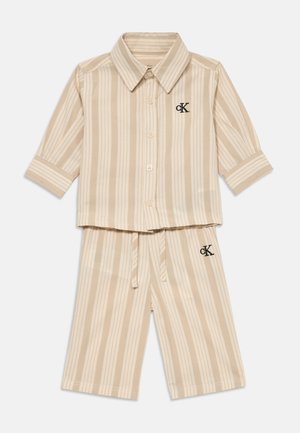 Beige és krém függőleges csíkos, rövid ujjú, gombos ing, hozzá illő, zsinórral állítható sorttal, mellyel a CK logók a mellkason és a combon találhatók.