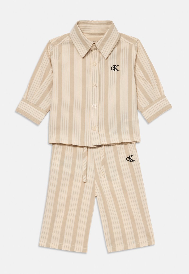 Béžová a krémová vertikálne pruhovaná košeľa s krátkym rukávom na gombíky a zodpovedajúce šortky na šnúrku s logami CK na hrudi a stehne.