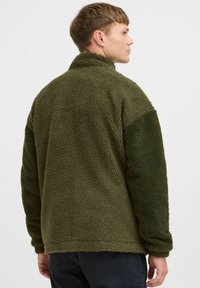 Olive green fleece pullover with a high collar, textured fabric, and contrasting sleeves. Relaxed fit with a smooth hem and cuffs.