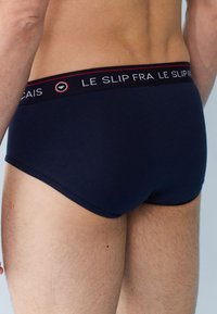 Marineblauwe katoenen slip met een contrasterende elastische tailleband waarop de tekst "LE SLIP FRANCAIS" in wit en rood staat, zachte textuur, aansluitend ontwerp.