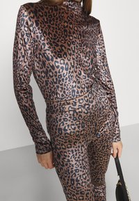 Body in stampa leopardata con toni brillanti di bronzo e nero, maniche lunghe, collo alto, design aderente, texture liscia, accompagnato da una borsa nera.