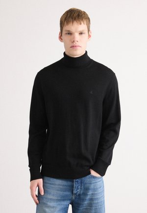 Zwarte coltrui van zachte stof, met een aansluitend ontwerp en geribde manchetten. Combinatie met lichtblauwe distressed jeans.