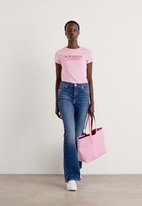 Rosa t-skjorte med "tommy jeans" logo, blå bukserskjorte, hvite sneakers og en rosa tote bag. Enkelt design med en glatt tekstur.
