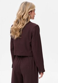 Burgundowa marynarka w prążki o skróconym kroju, z długimi rękawami i dopasowaną sylwetką. Gładka tkanina o subtelny połysku.