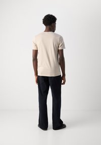 Tricou bej cu mânecă scurtă, cu guler rotund, asociat cu pantaloni drepti de culoare albastră închis. Textură de stofă netedă, design simplu, fără modele.