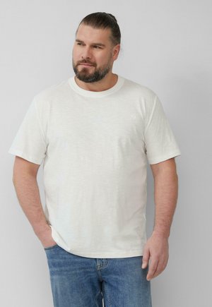 Weißes Baumwoll-T-Shirt mit kurzen Ärmeln, Rundhals und leichter Textur. Kombiniert mit blauen Jeans. Einfaches Design mit minimalem Branding.