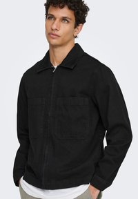 Μαύρο τζιν μπουφάν με γιακά, μπροστινό φερμουάρ και δύο τσέπες στο στήθος. Διαθέτει άνετη γραμμή και ανθεκτική υφή υφάσματος.