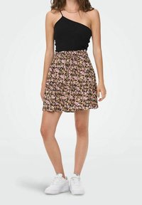 Top asimmetrico nero abbinato a una gonna floreale nera con fiori rosa e viola, lunga fino sopra il ginocchio, indossato con sneakers bianche.