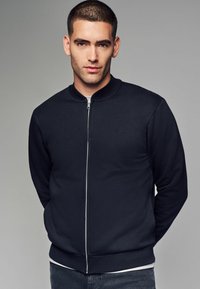 Veste bomber bleu marine avec une fermeture éclair frontale, un col, des poignets et un ourlet côtelés. Le matériau est lisse, offrant un design ajusté sans motifs.