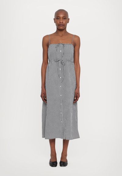 Schwarz-weißer Gingham-Midi-Kleid mit Spaghettiträgern, tailliertem Schnitt, Knopfleiste und lockerer Passform, kombiniert mit schwarzen Ballerinas.