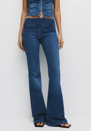 Denim flared jeans in dark blue, featuring a fitted waist, soft texture, and slight stretch, paired with a cropped denim top.