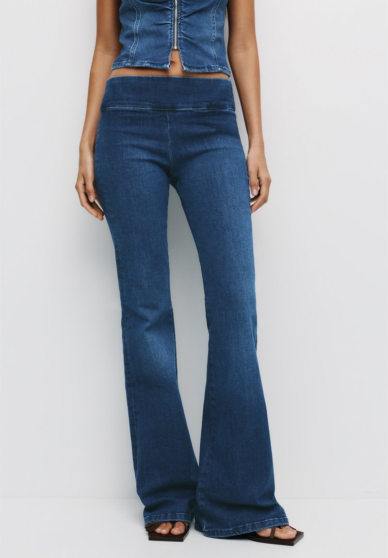 Donkerblauwe denim flared jeans met een aansluitende taille, zachte textuur en lichte rek, gecombineerd met een cropped denim top.