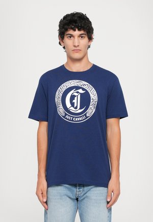 Tricou din bumbac bleumarin, cu un logo circular alb cu model de șarpe și textul "Just Cavalli" în centru. Mâneci scurte, croială relaxată.