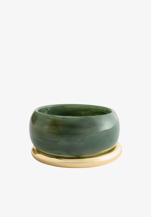 Bred, mørkegrøn jade-armring med glat poleret overflade, der hviler på en rund, skinnende guldfarvet base på hvid baggrund.